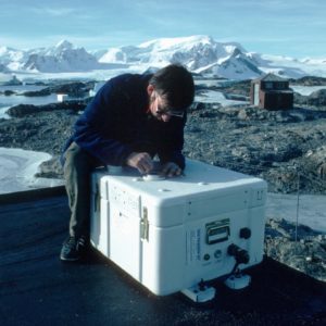 SAOZ - observes spectra of UV and visible sunlight scattered from the zenith sky at twilight, to measure total column ozone and Nitrogen dioxide. SAOZ (Systeme d'Analyse d'Observations zenithales) is in a weather-proof box and looks up through the simple quartz window in its lid. Derek Oldham is seen here installing SAOZ on the roof of the ozone loft in March 1990. Faraday station was occupied by BAS from 1947 to 1996, it was transferred to the Ukraine in February 1996 and renamed Vernadsky. SAOZ was moved to Rothera when Faraday was transferred to the Ukraines