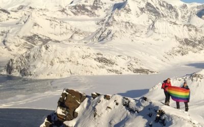 People on a snowy mountain range holding a rainbow flag