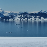 Skis in snow with body of water against snow covered mountains