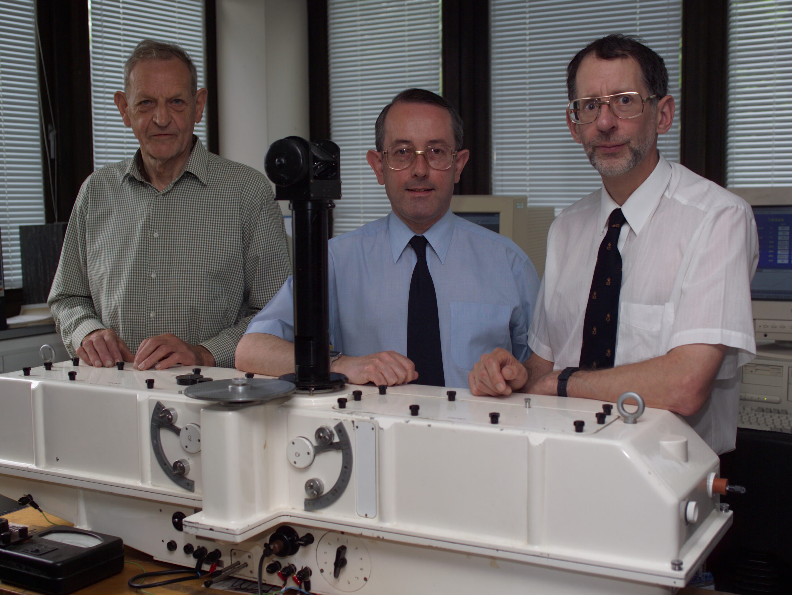 Three men standing behind a scientific instrument